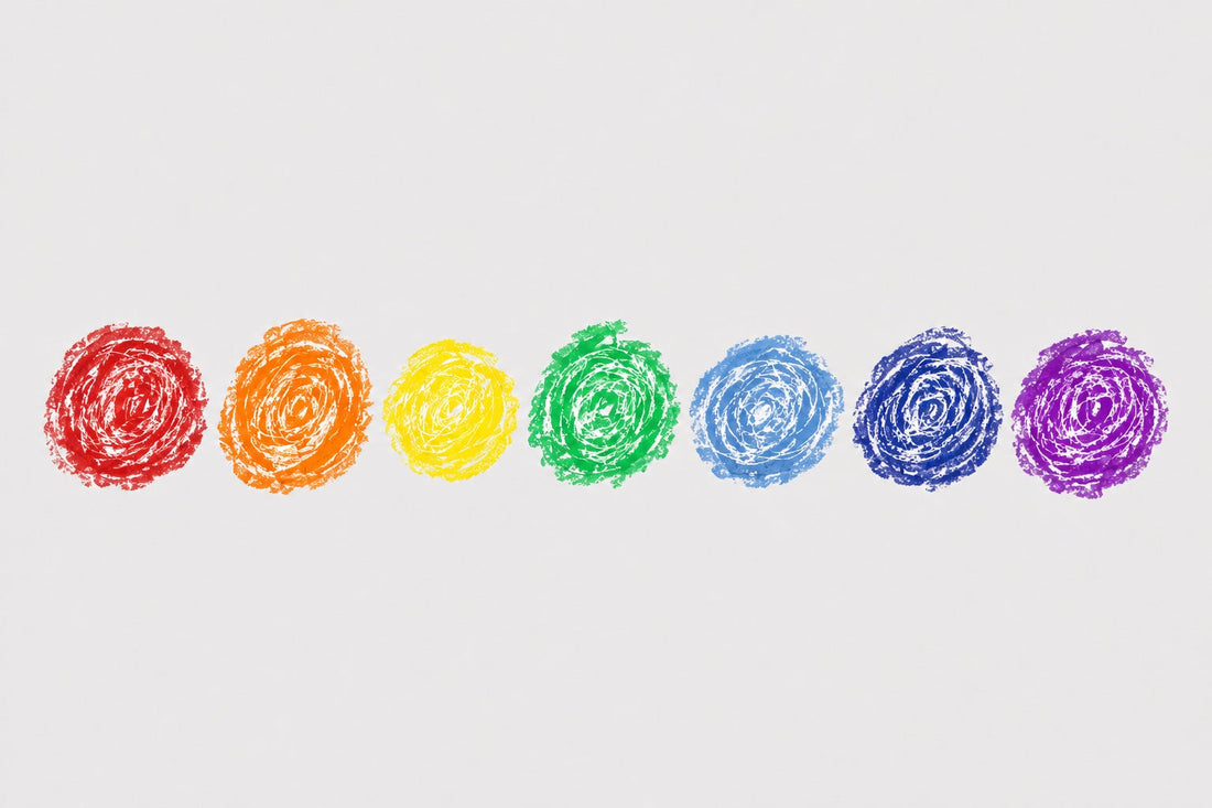 Seven hand-drawn crayon circles in the rainbow chakra colours, red to violet, in a row on grey paper